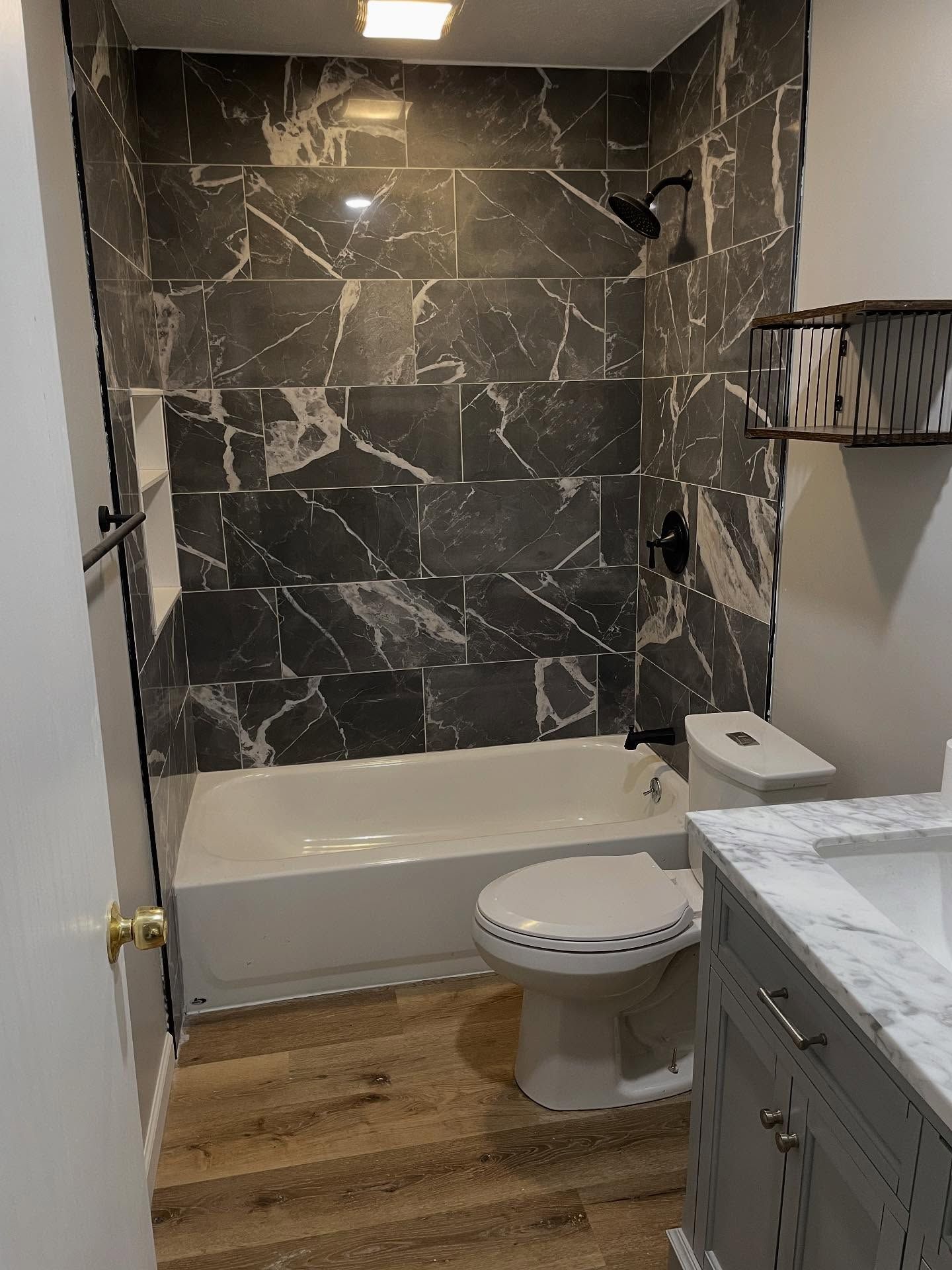 Accessible bathroom with tub, toilet, vanity, dark marble shower wall, and wood-look floor