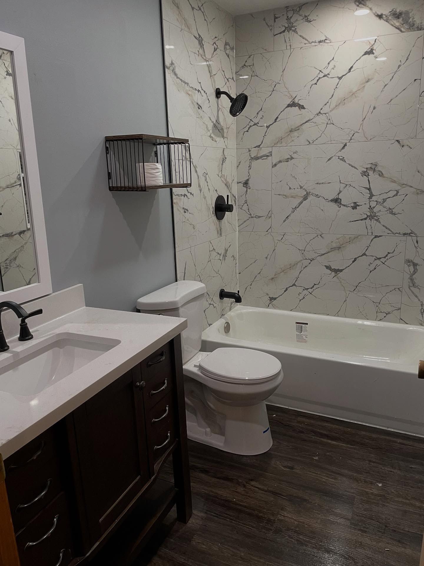 Bathroom with white tub, toilet, and vanity against gray walls and dark wood floor.