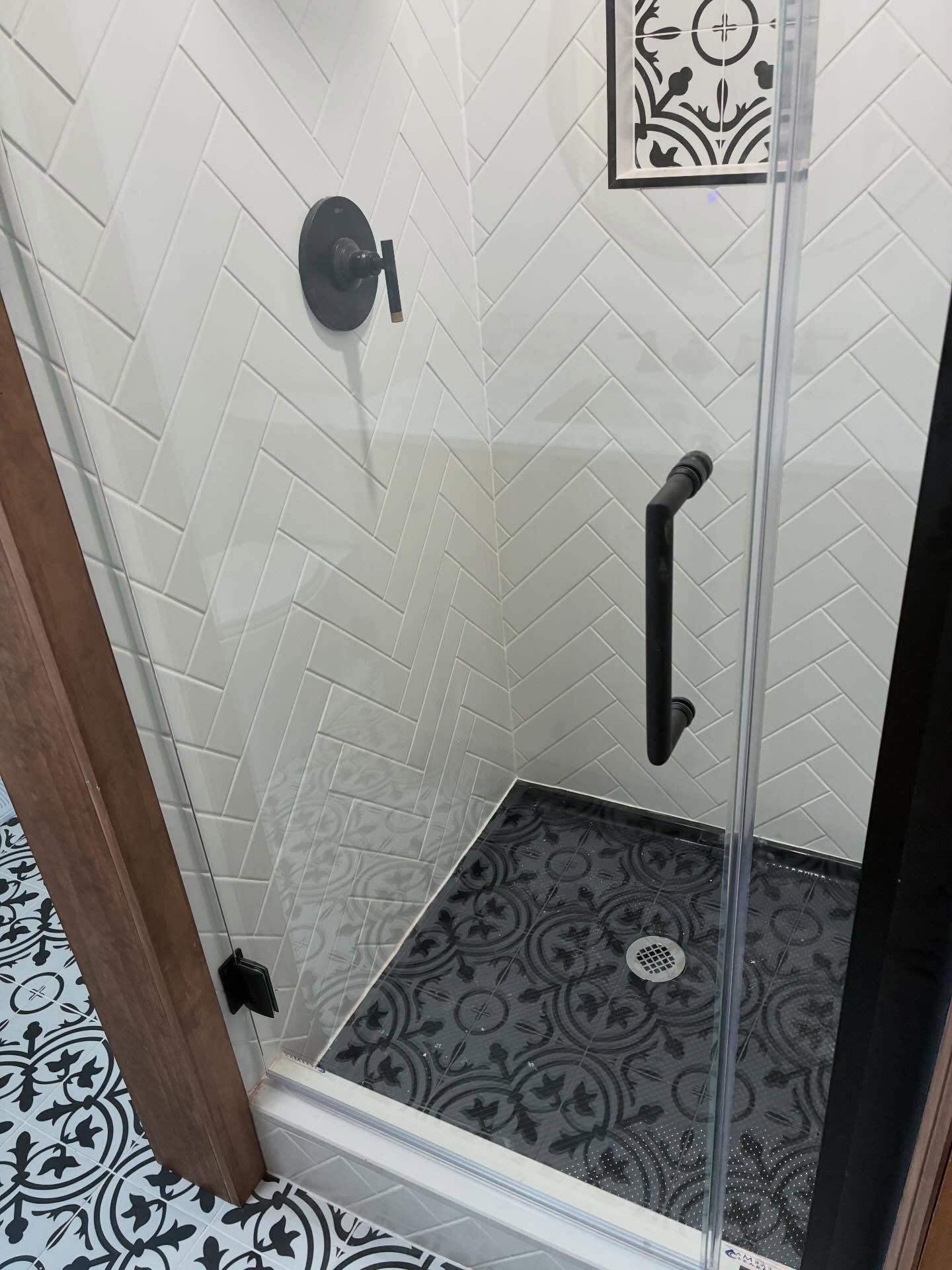 Small shower stall with black floor tile, white walls, grab bar, and rainfall showerhead.