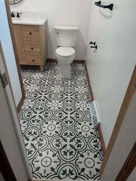Small bathroom with patterned tile floor, toilet, wood vanity, and white walls.
