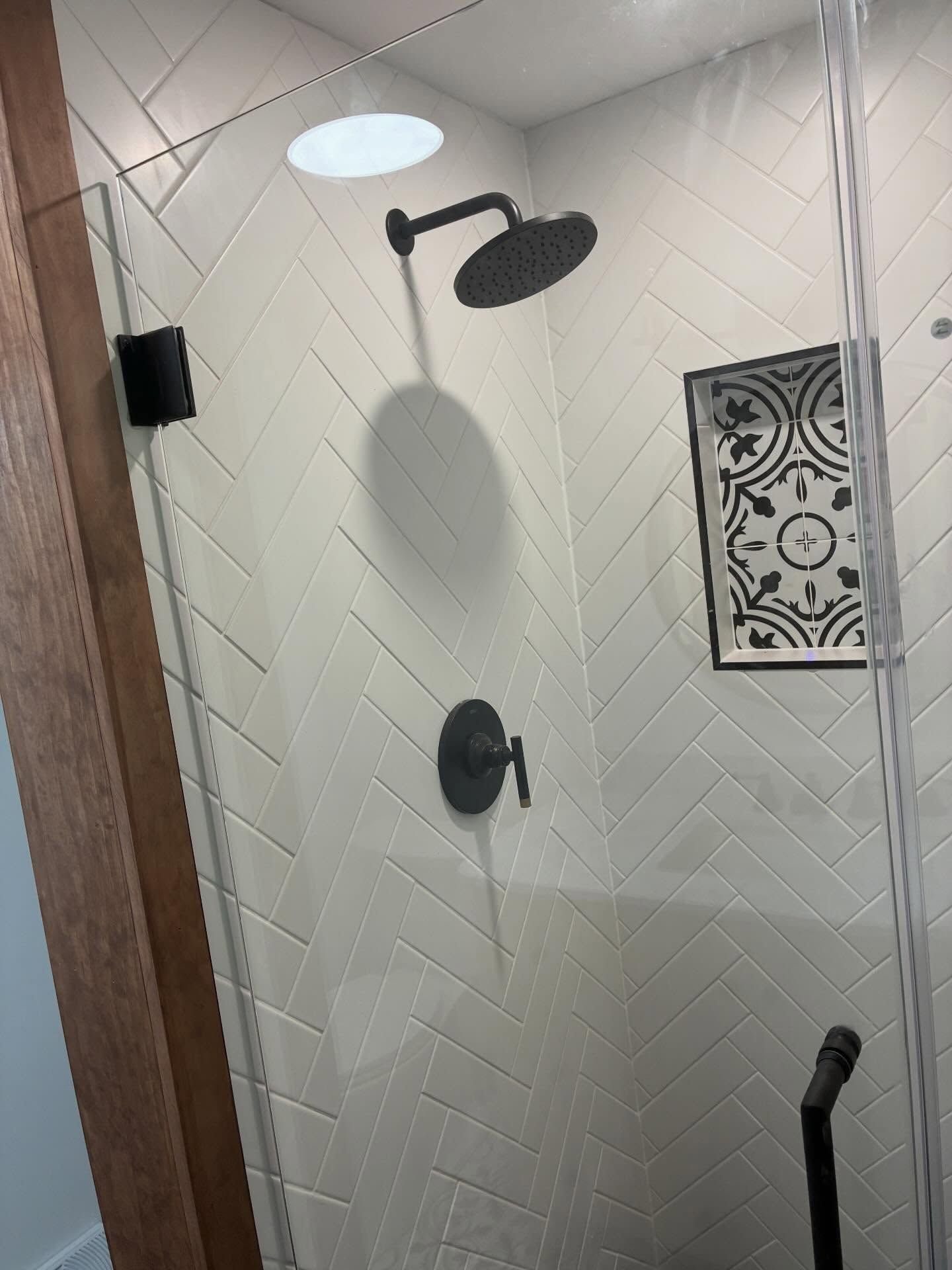 Bathroom shower stall with dark fixtures, white tile walls, and a decorative wall accent.