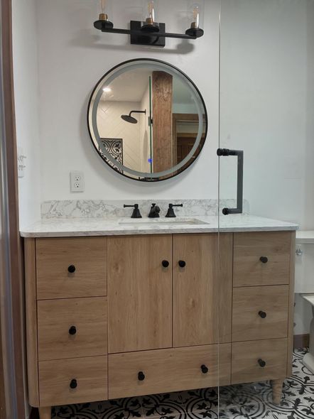 Modern wooden bathroom vanity with round mirror, black fixtures, and white marble countertop