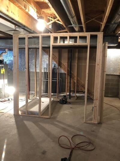 Unfinished basement framed with wood studs, exposed ceiling joists, and a coiled hose on the concrete floor.
