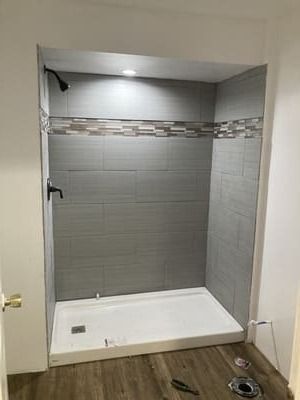 Empty tiled shower stall with gray accent wall and white shower base in a bathroom