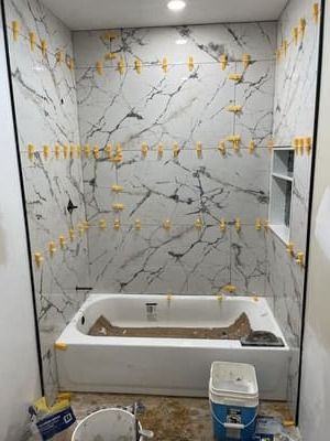 Tiled bathroom under renovation with a bathtub, paint buckets, and a ladder.