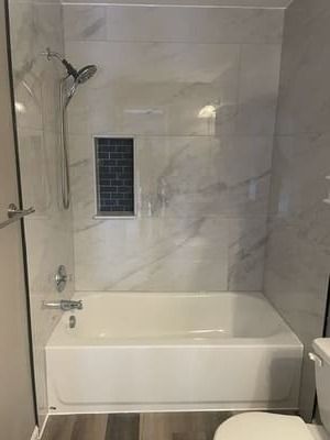 Modern bathroom with a bathtub, tiled walls, showerhead, and small window.