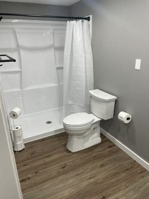 Small bathroom with a shower-tub, toilet, and gray walls with wood-look flooring.