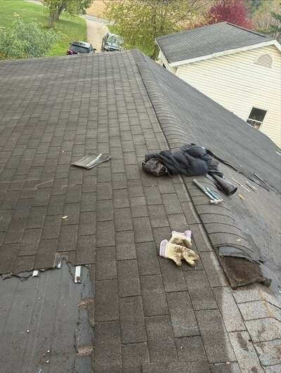 Rooftop shingles damaged by a storm, with loose debris and a bag on the roof slope.