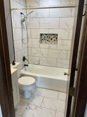 Compact beige-tiled bathroom with toilet, tub shower, and wall niche.