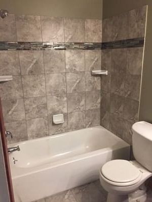 Small bathroom with tiled shower-tub, toilet, and beige walls and fixtures.