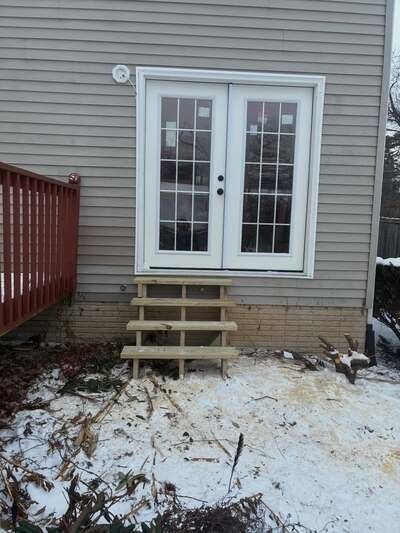 Back door with white French doors, three wooden steps, and a snowy patio beside a red railing