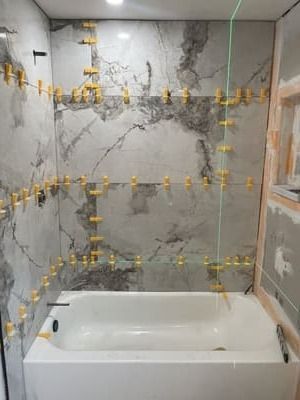 Partially tiled bathroom shower with a white bathtub and wall leveling clips exposed