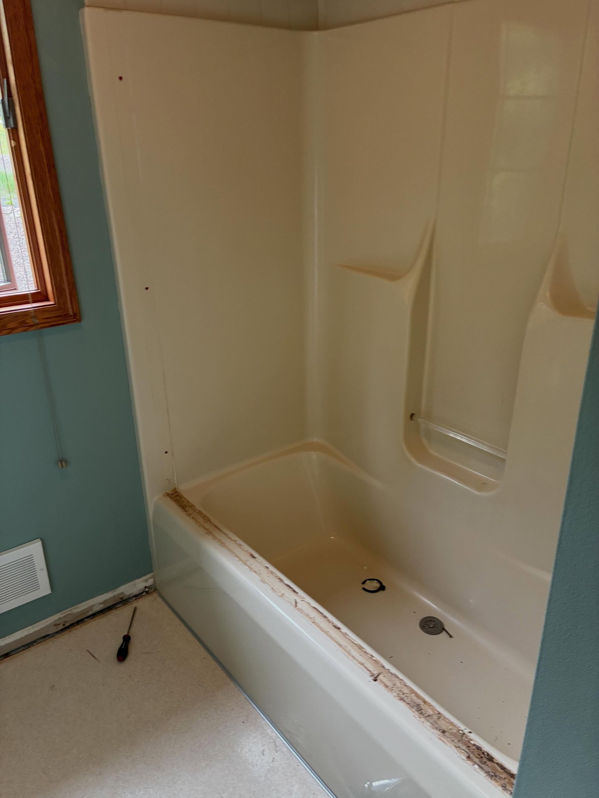 Small bathroom with a beige walk-in bathtub and shower wall, next to a window and green painted wall.