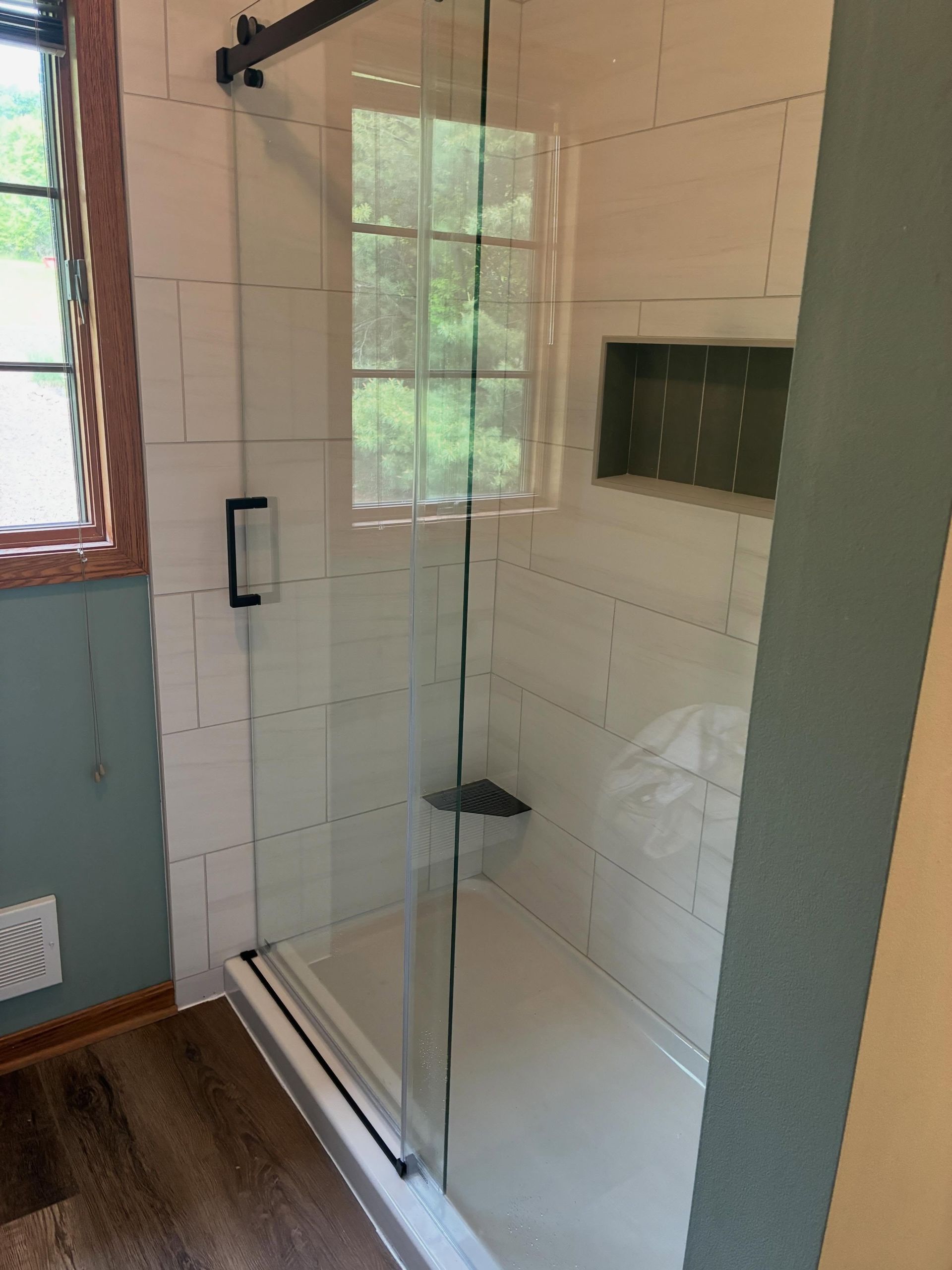 Glass walk-in shower with black fixtures and a tiled interior in a bathroom