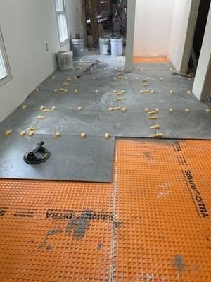 Partially renovated hallway with gray floor and orange underlayment, scattered debris, and a black tape roll