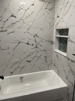 Small bathroom with white marble-patterned tile walls, a white bathtub, and a small frosted window.