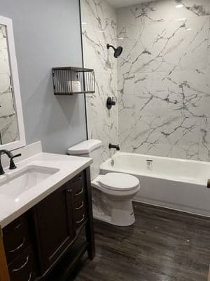 Modern bathroom with dark vanity, white tub and marble shower wall, plus toilet and mirror