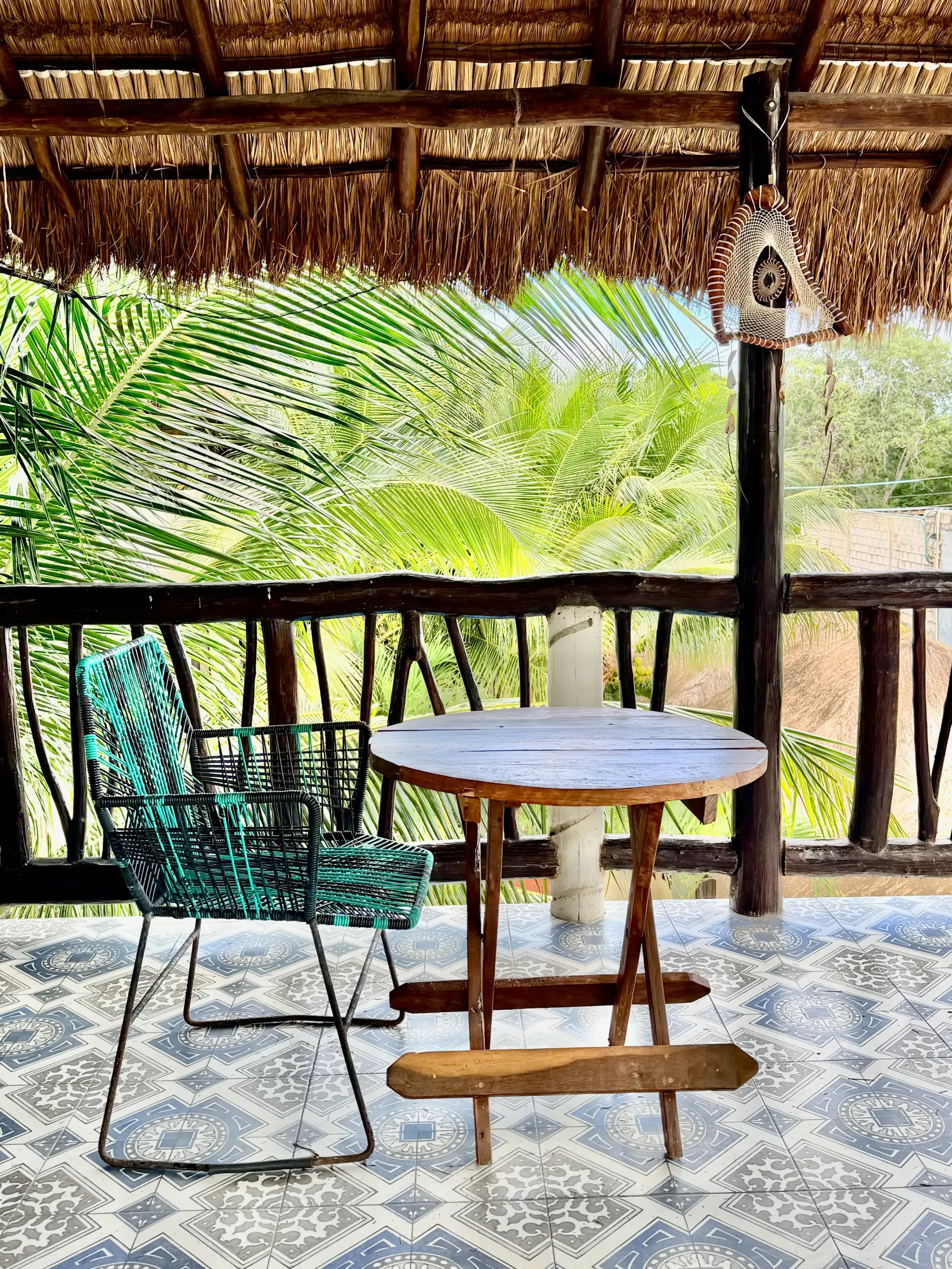 Small round table and green wire chair on a shaded porch with tropical greenery beyond