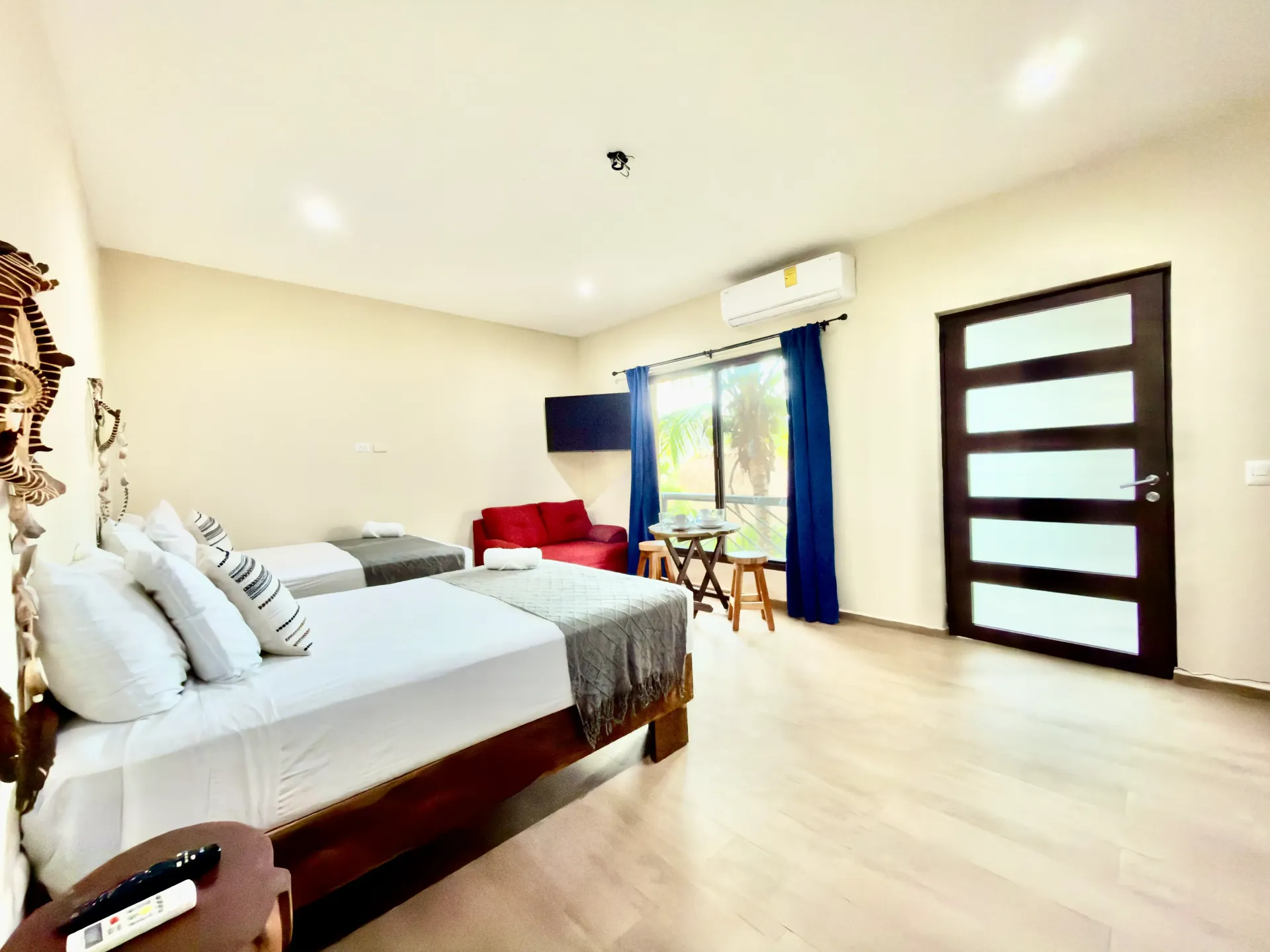 Bright bedroom with two beds, white walls, wooden floor, blue curtains, and a door with frosted glass panels