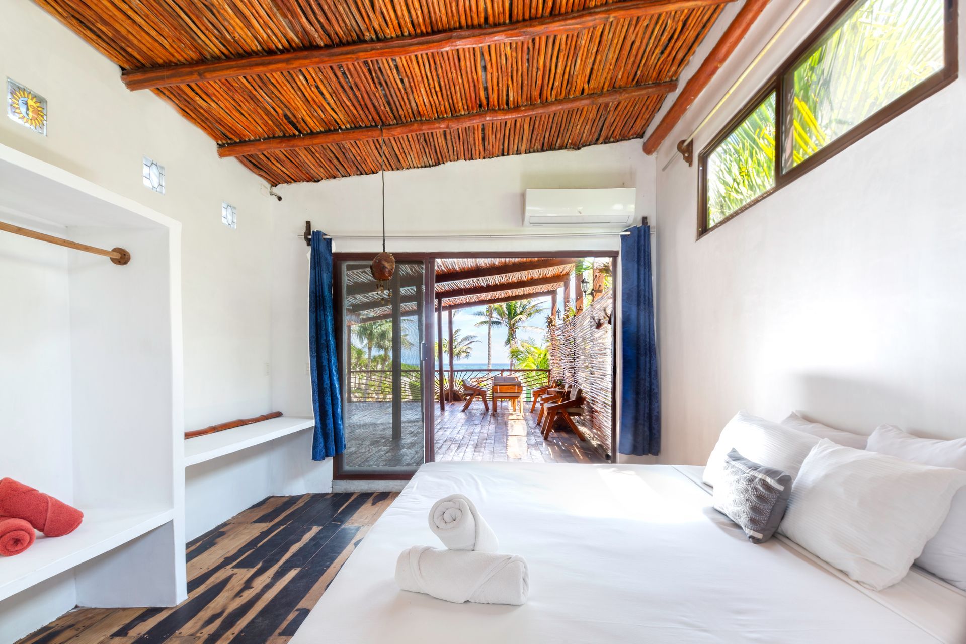 Bright white bedroom with wooden ceiling, open glass doors, and a view to a patio and greenery.
