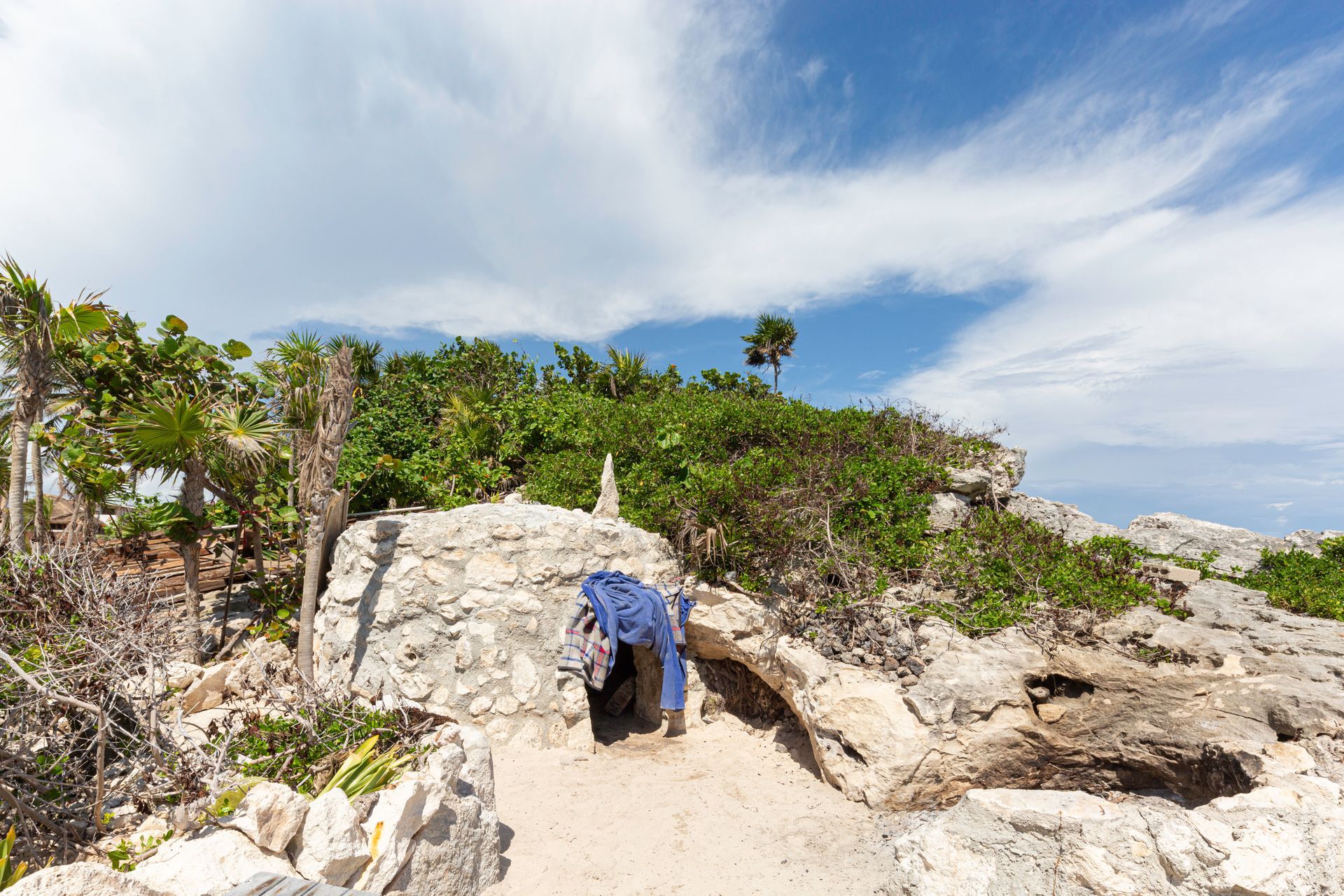 Person in blue shirt bending under a rocky cave on a sunny tropical hillside