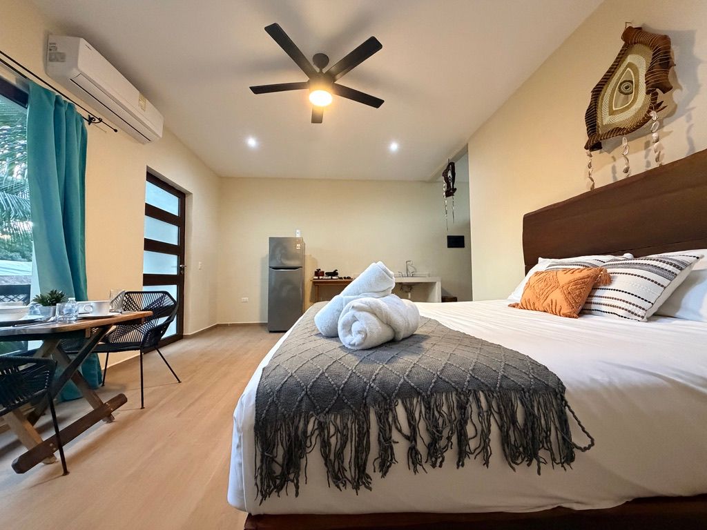 Bright bedroom with king bed, ceiling fan, teal curtains, desk, and wall-mounted TV