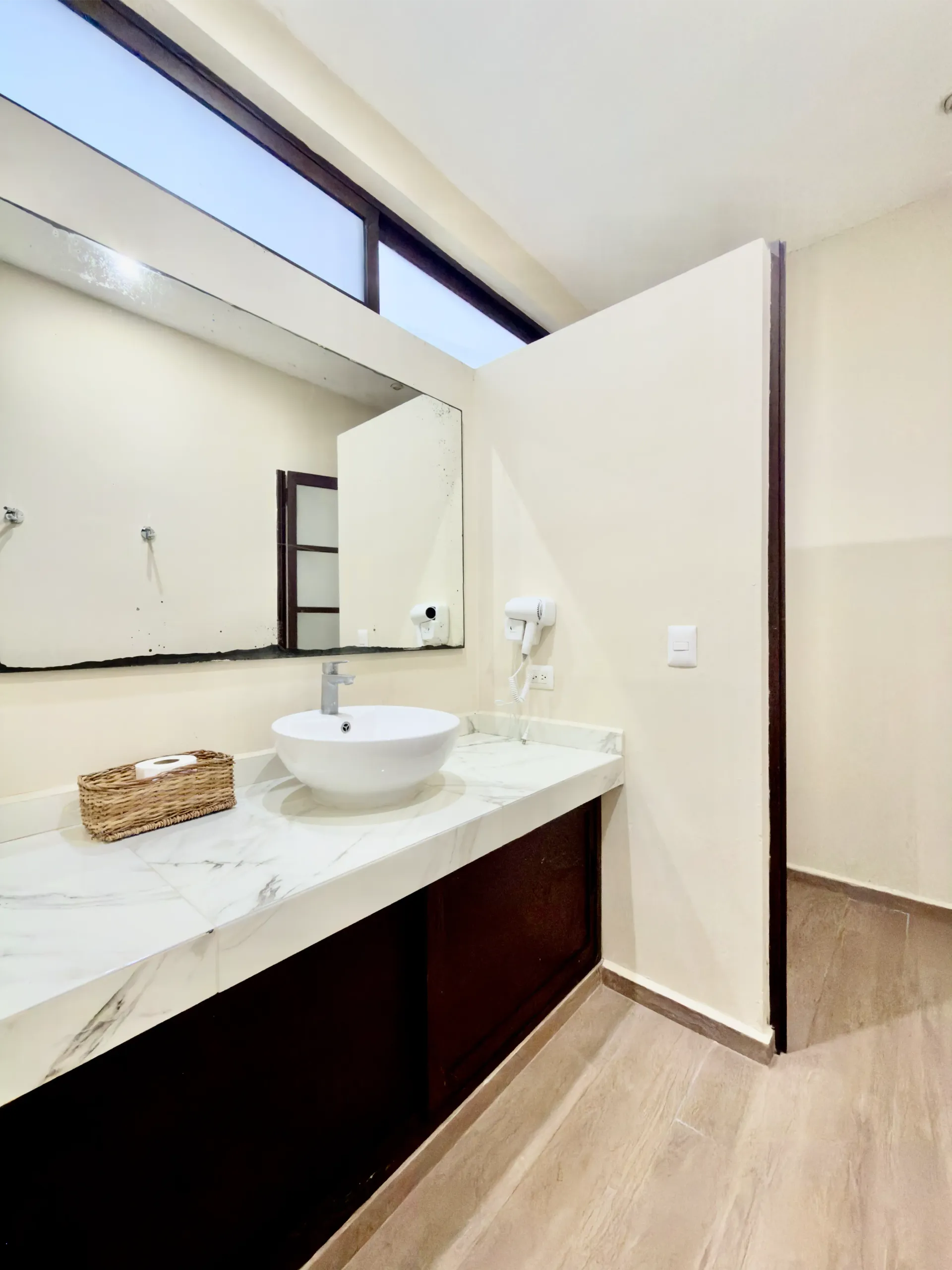 Modern bathroom vanity with white countertop, round sink, mirror, and wood flooring