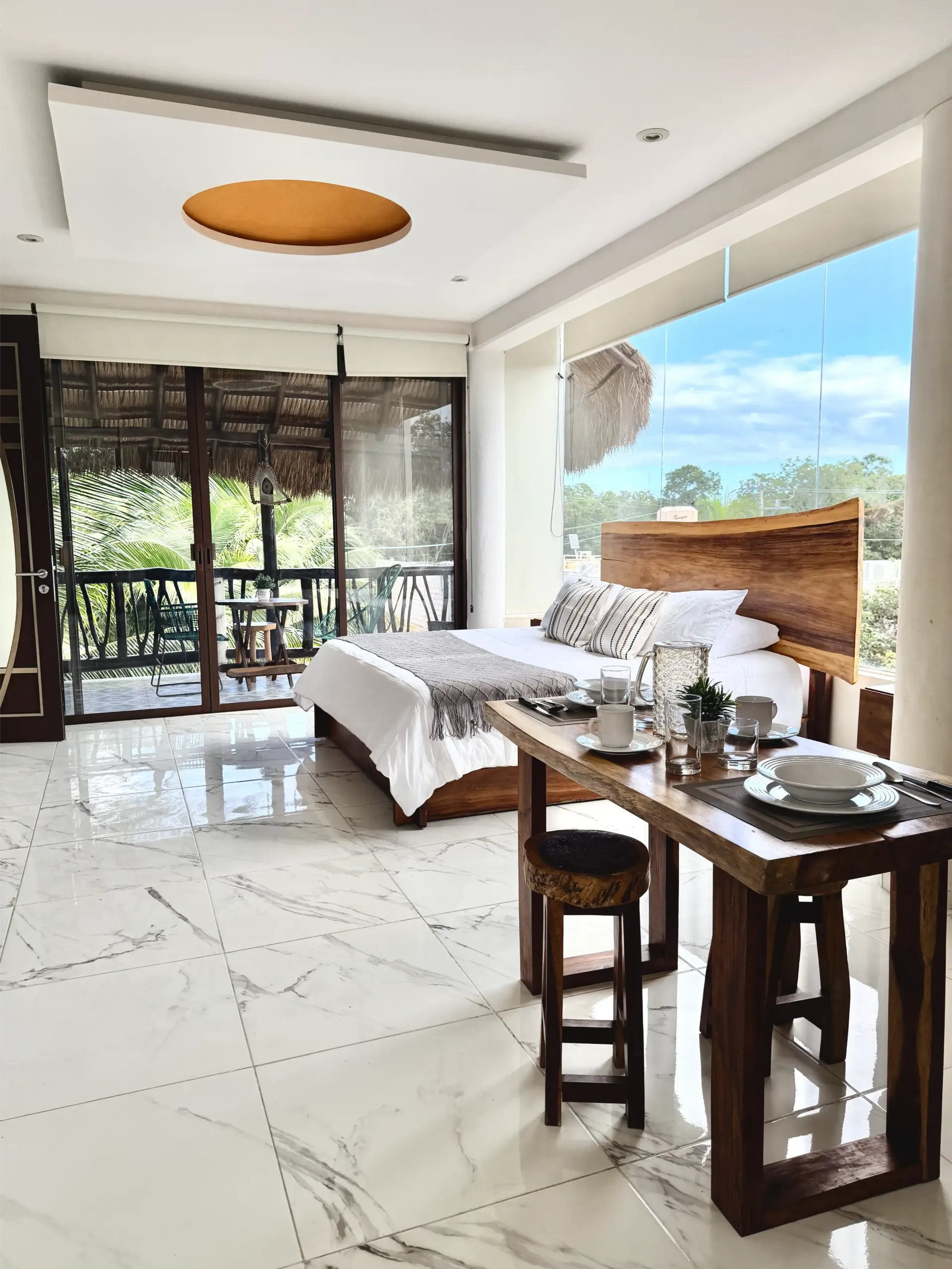 Bright modern bedroom with a bed, wooden desk, large windows, and ocean view