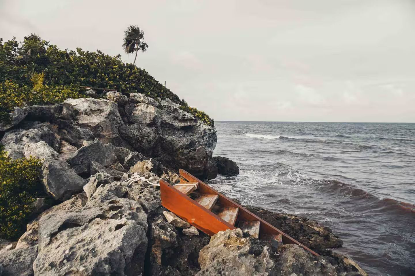 Orange canoe wedged among rocky coastal cliffs beside a rough gray sea