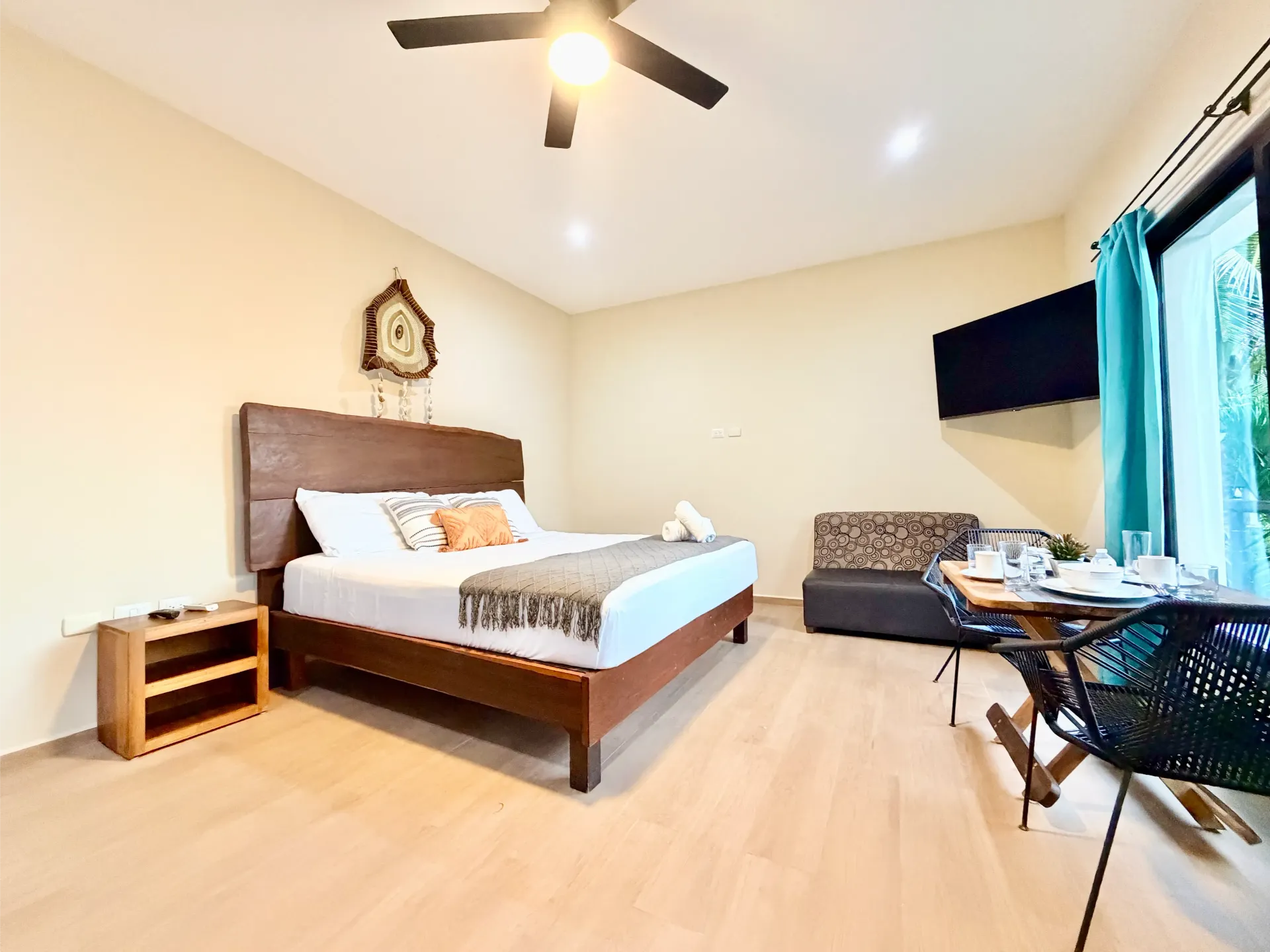 Bright bedroom with a wooden bed, ceiling fan, light wood floor, and window with curtains