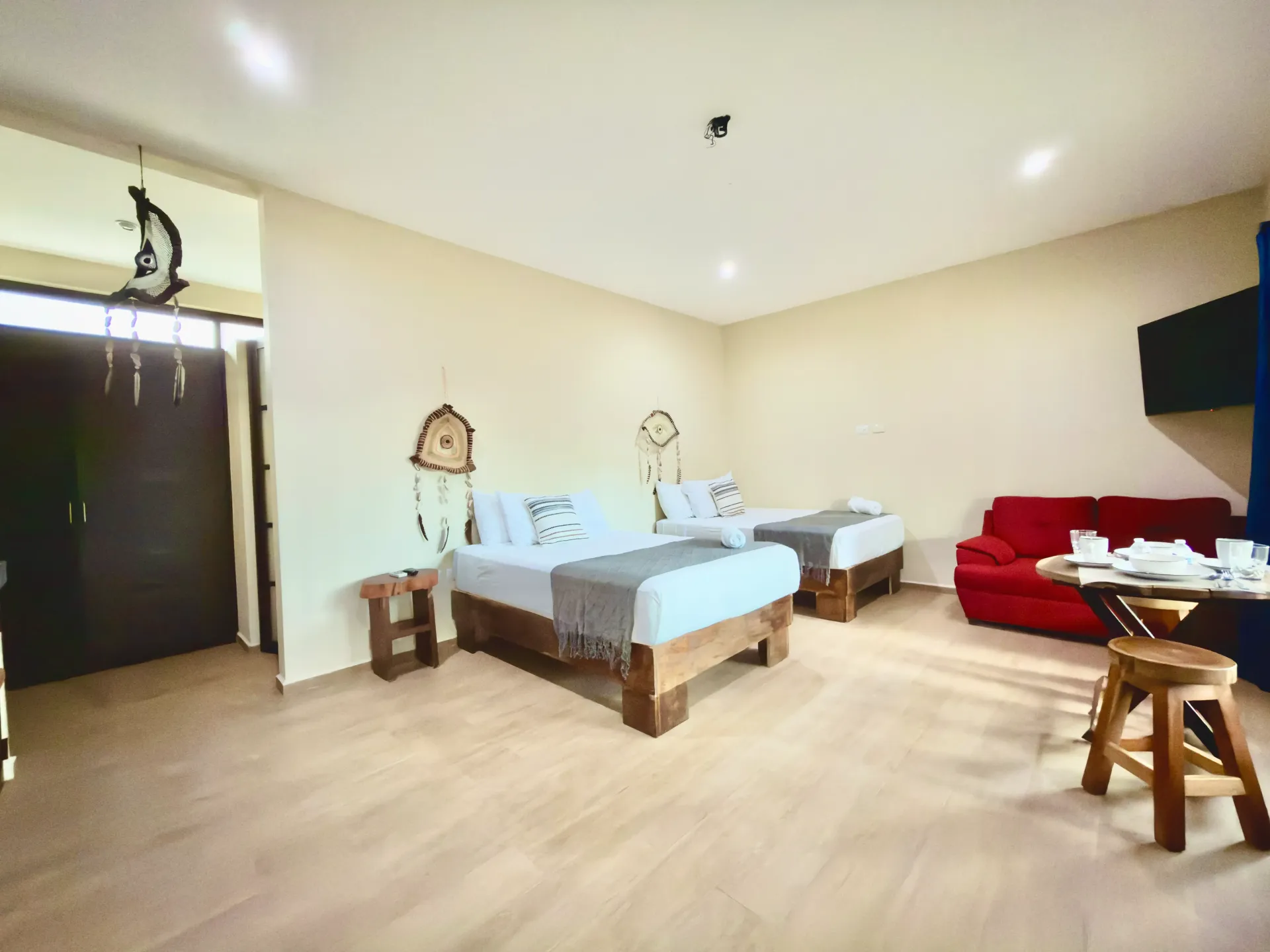 Spacious bedroom with two twin beds, a red sofa, a small table, and dark sliding doors on a light wood floor.