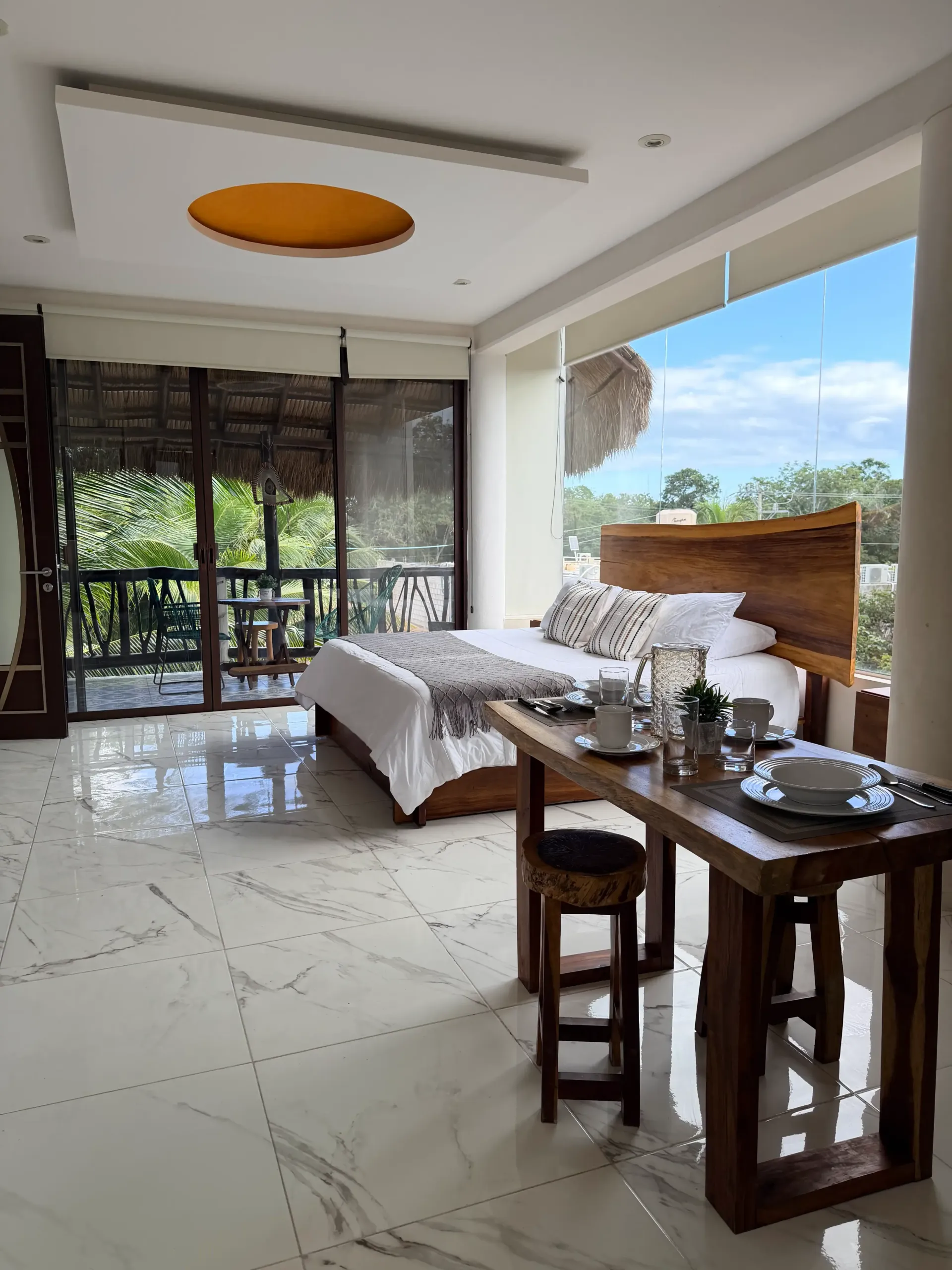 Modern living room with sofa, dining table, glossy floor, and large windows overlooking greenery.