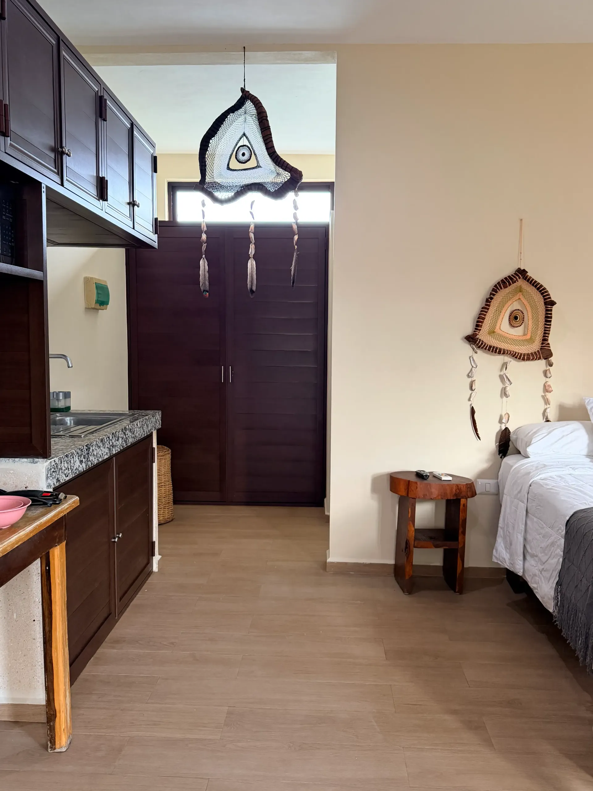 Small room with kitchen cabinets, wooden doors, a bed, and wall hangings on a wood floor.