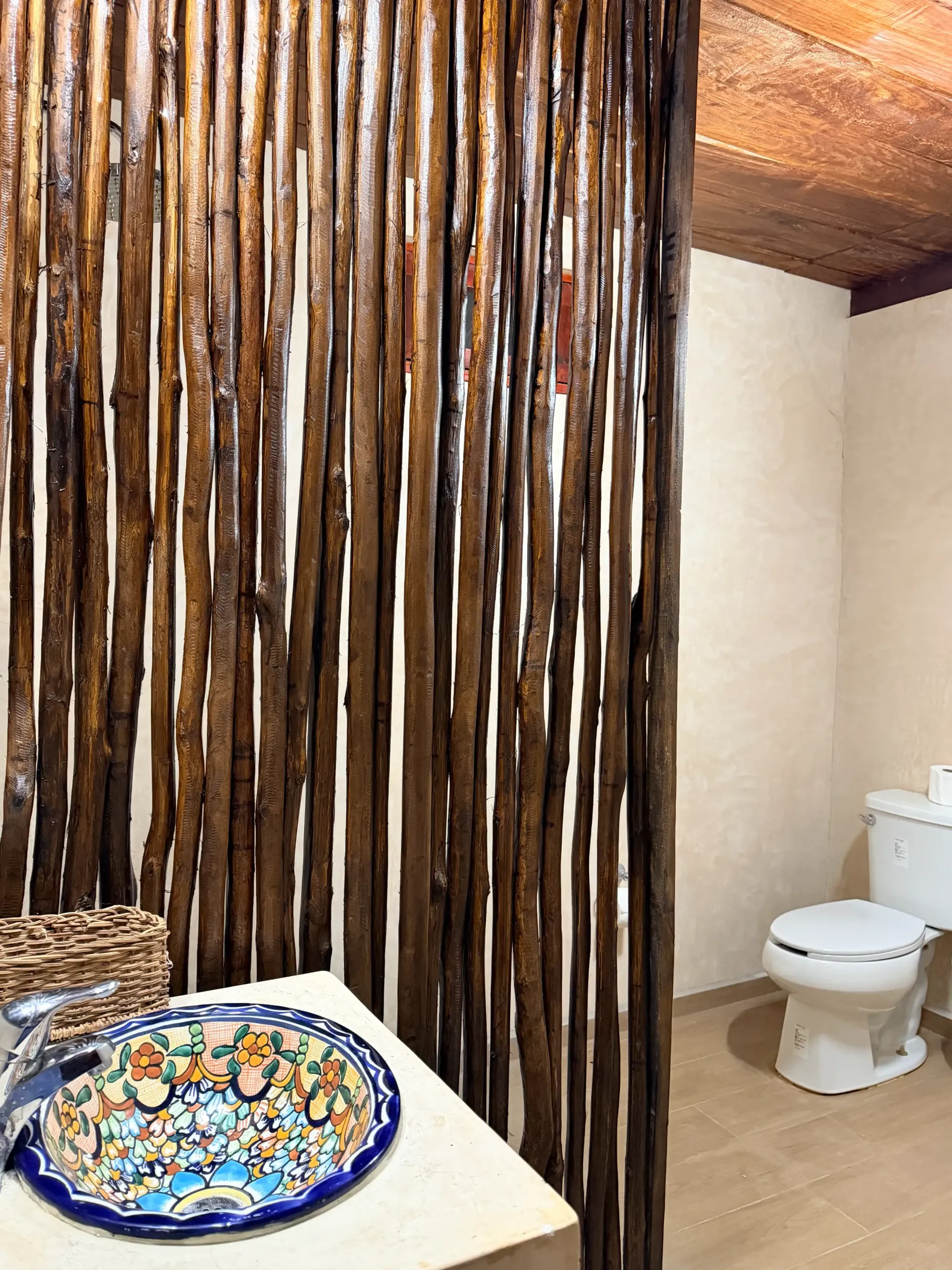 Rustic bathroom with bamboo wall, white toilet, and colorful mosaic sink counter