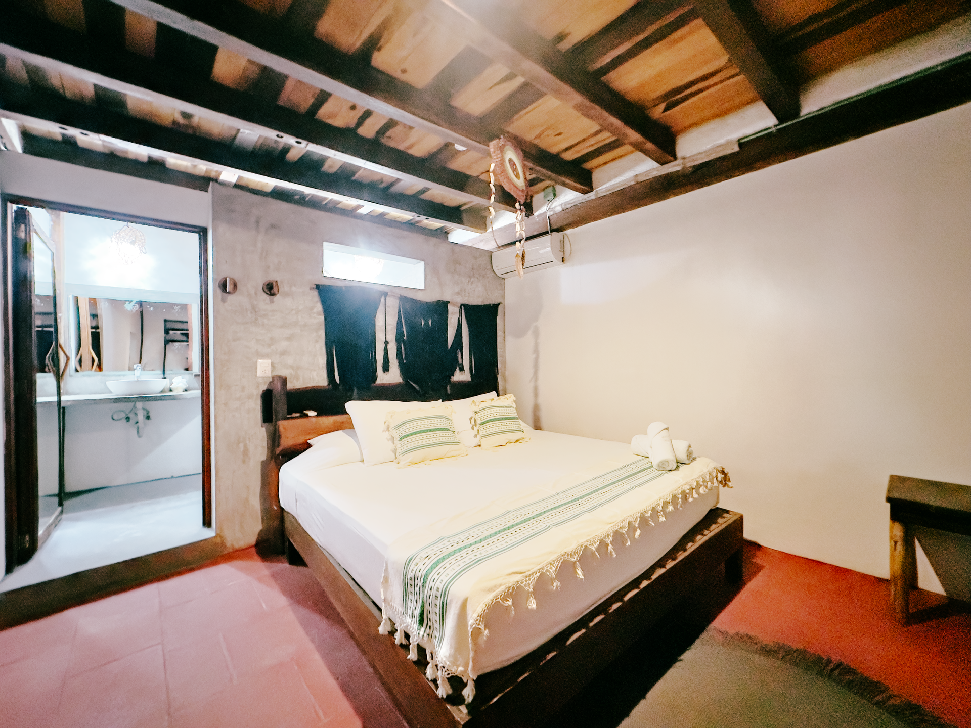 Cozy bedroom with a bed, exposed wooden ceiling beams, and an adjoining bathroom doorway