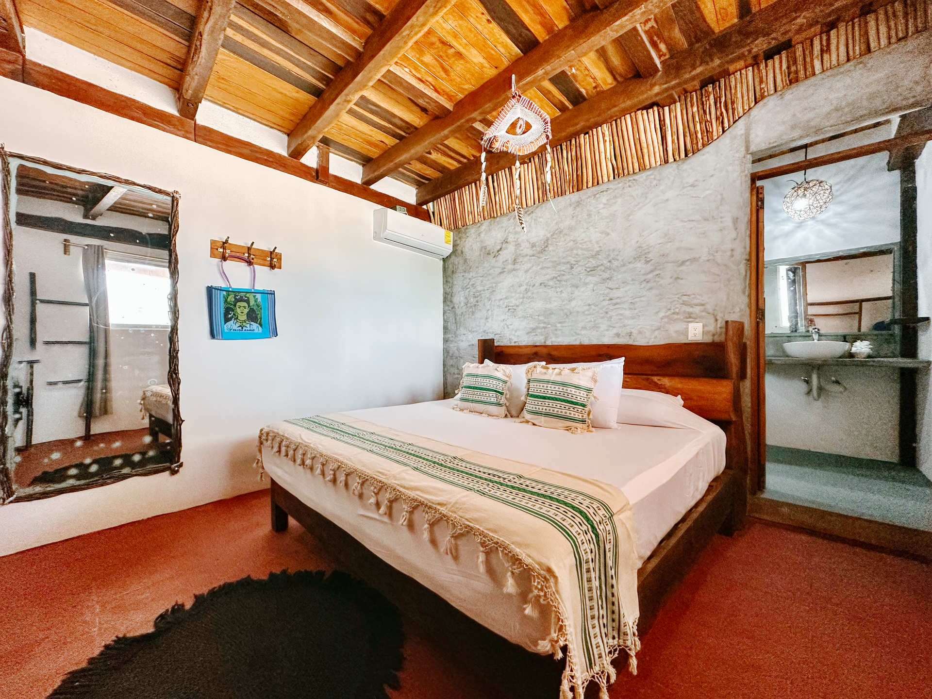 Rustic bedroom with wooden bed, white walls, exposed beam ceiling, and wall mirrors