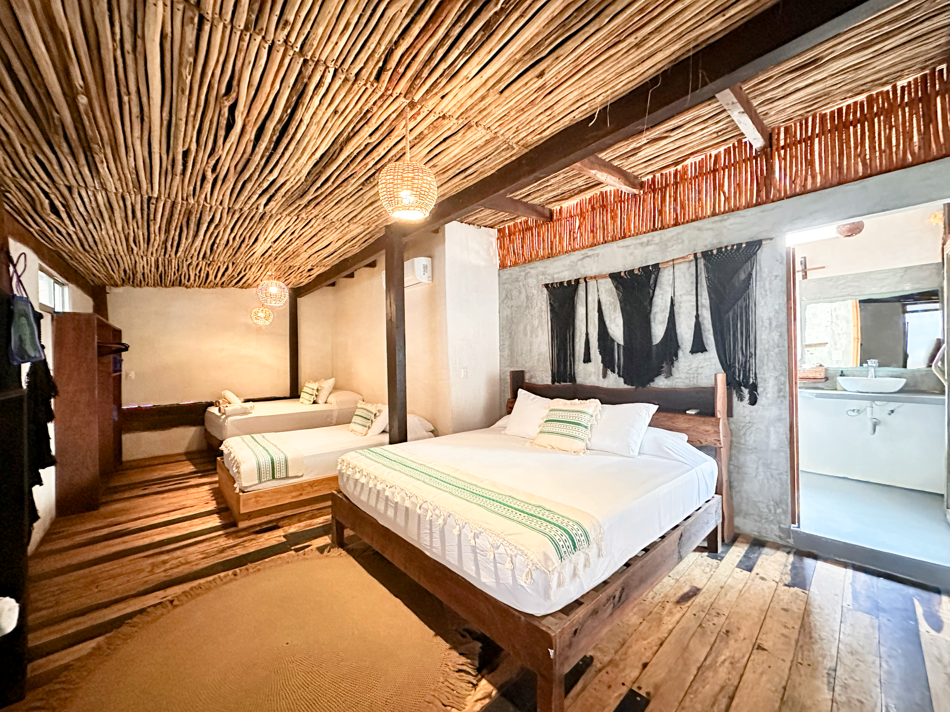 Rustic bedroom with two beds, woven ceiling, and wooden floors, lit by warm natural light