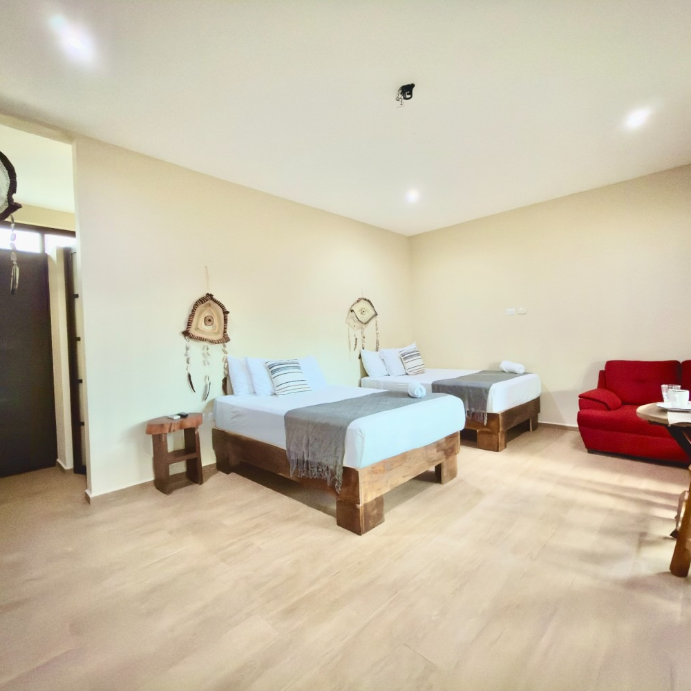 Bright bedroom with two beds, cream walls, light wood floor, and a red armchair.