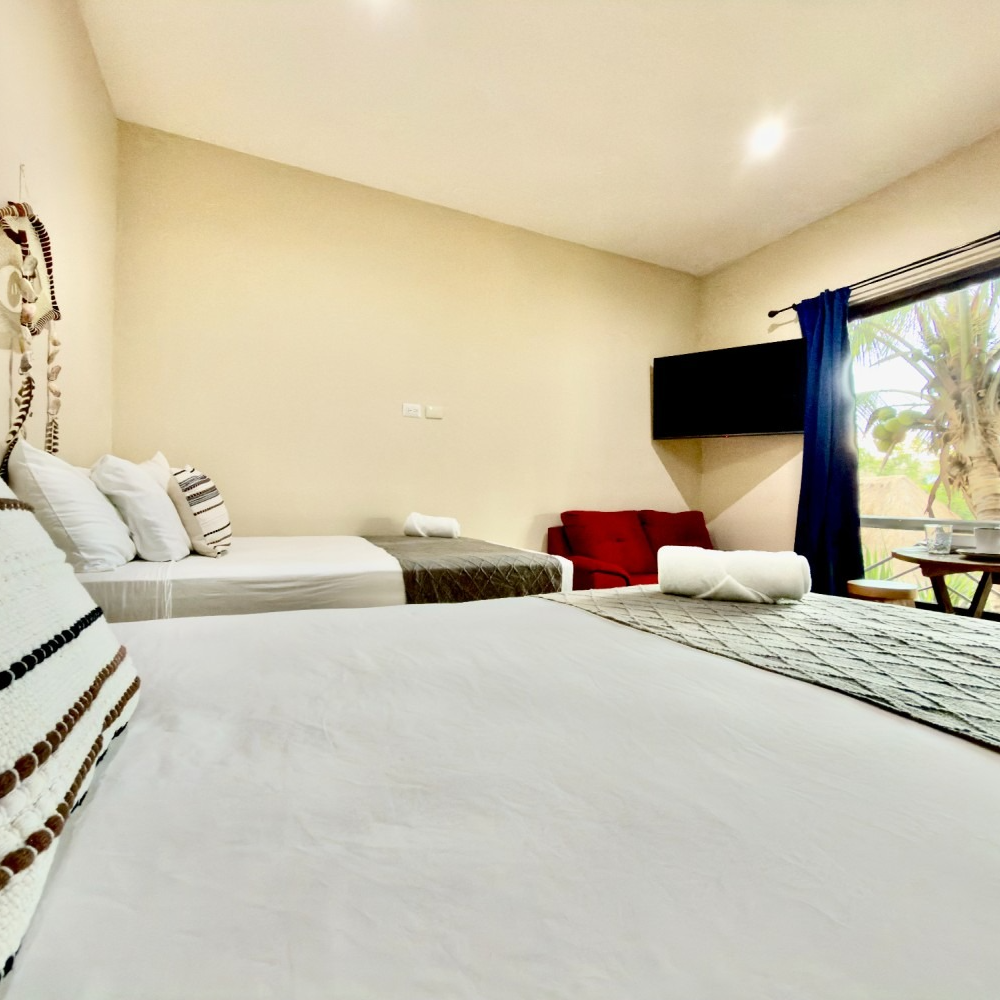 Bright bedroom with two beds, white linens, a red chair, and a window with blue curtains