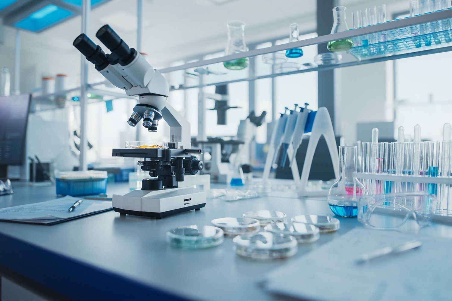 Microscope in a bright laboratory with glassware and test tubes on a workbench