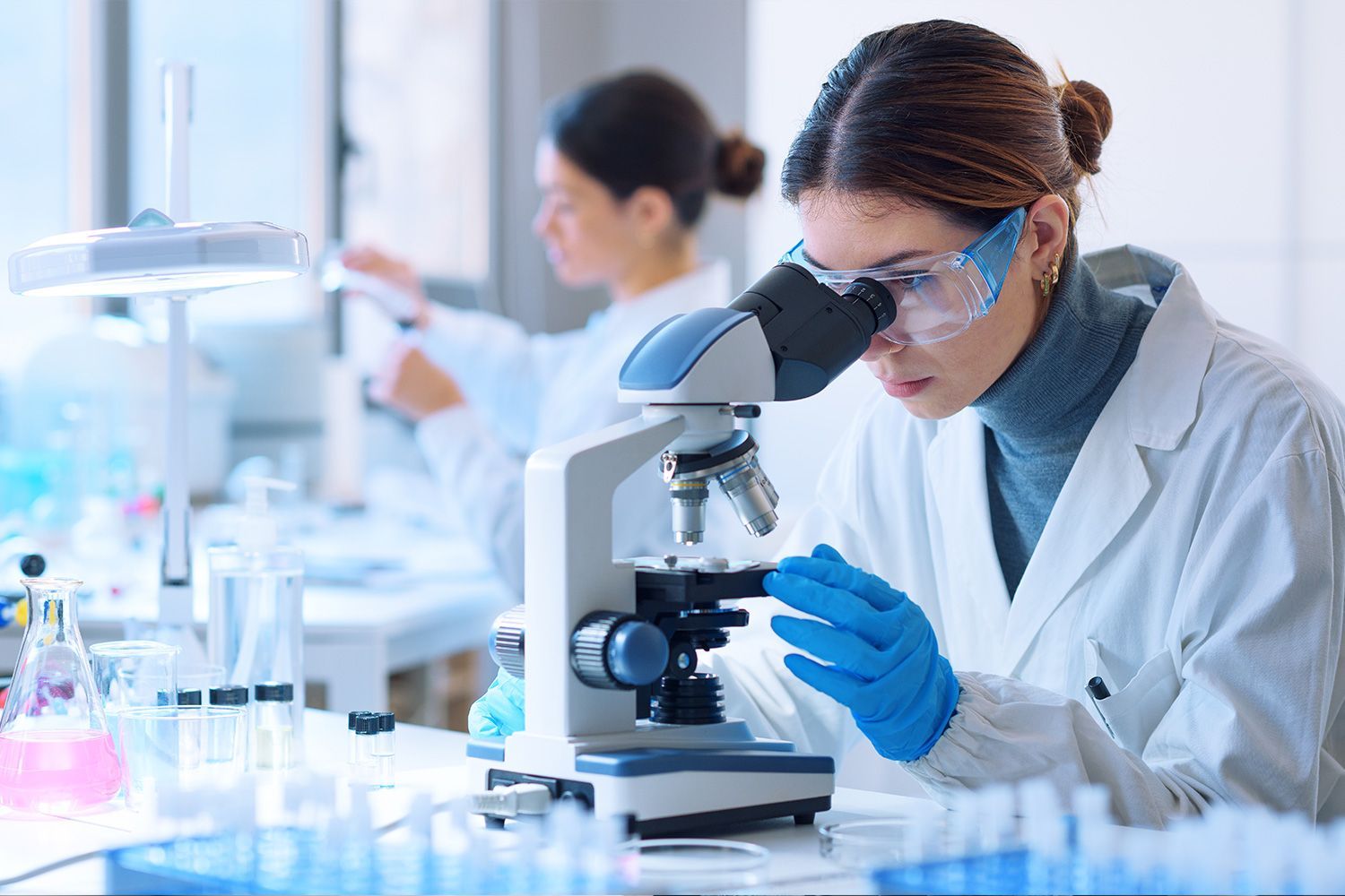 Scientist in blue gloves examining a sample through a microscope in a bright laboratory