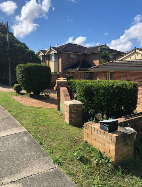 Charming Brick House with Black Fence in Pristine Garden Setting — Craig’s Lawn Mowing and Garden Maintenance in Miranda, NSW