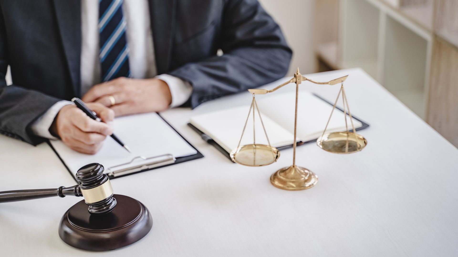 Lawyer writing at desk with gavel, scales of justice, and documents.
