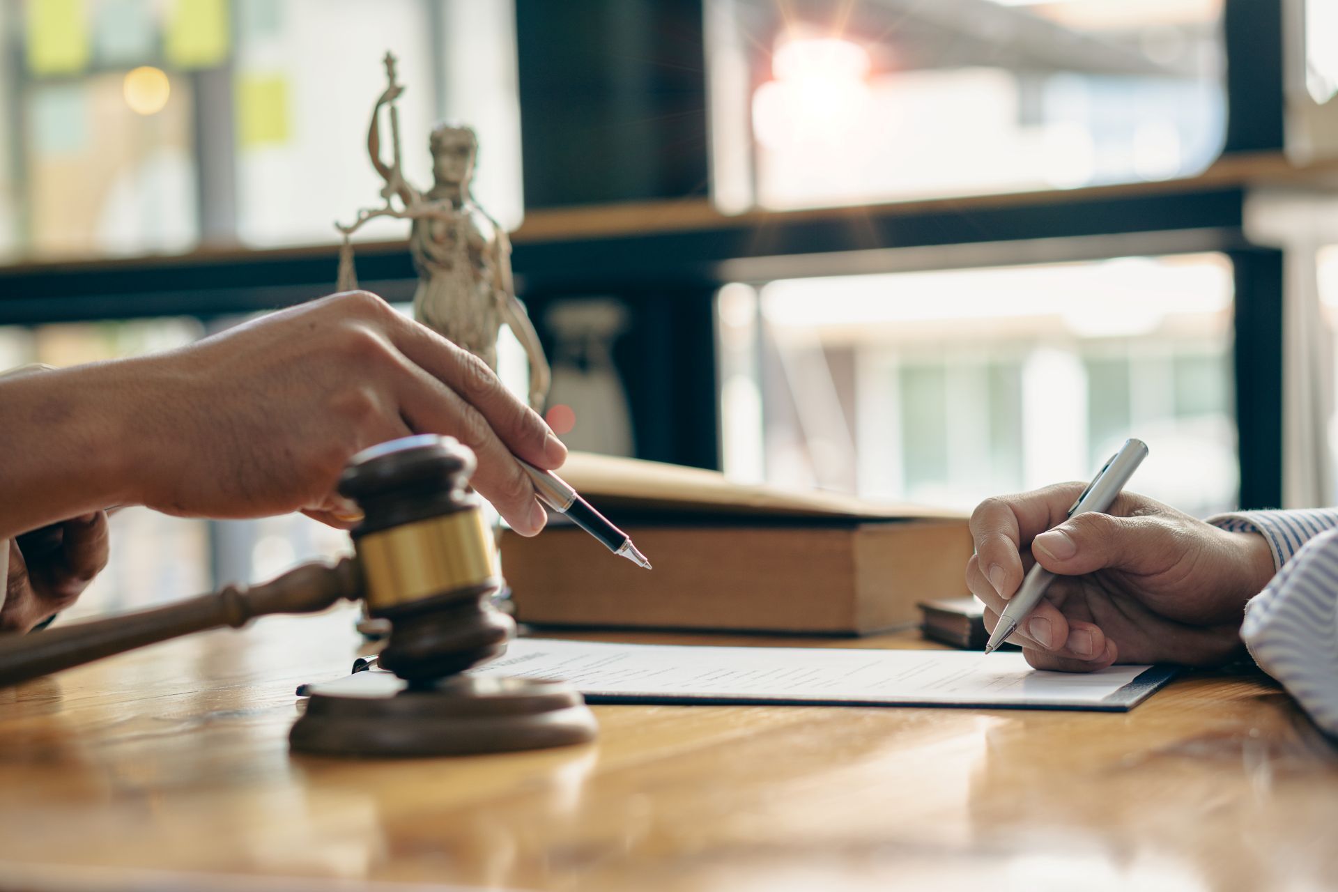 Hands pointing to document, gavel, statue of justice on desk, signing a document.