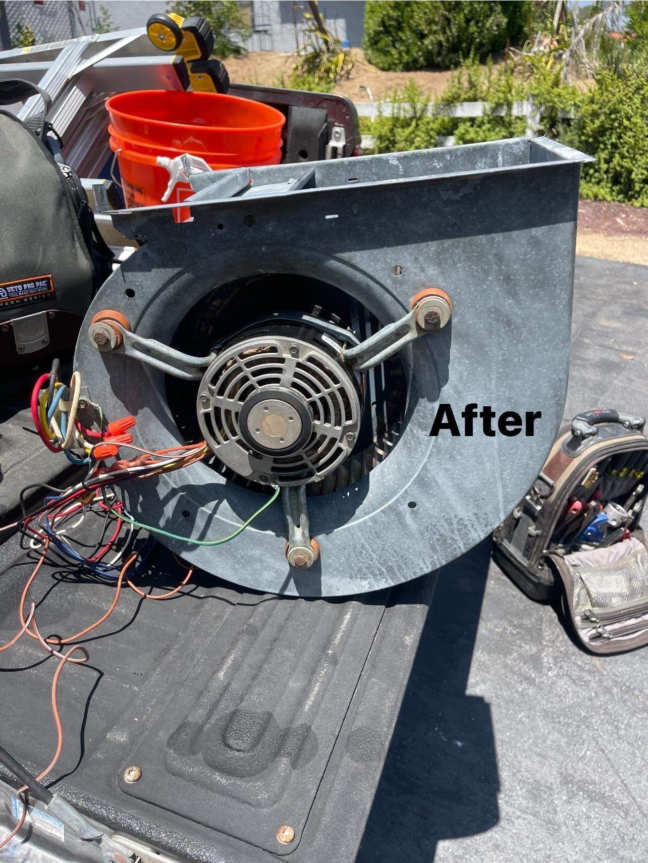 Air handler fan unit on truck bed with wires, tools, and bucket visible.