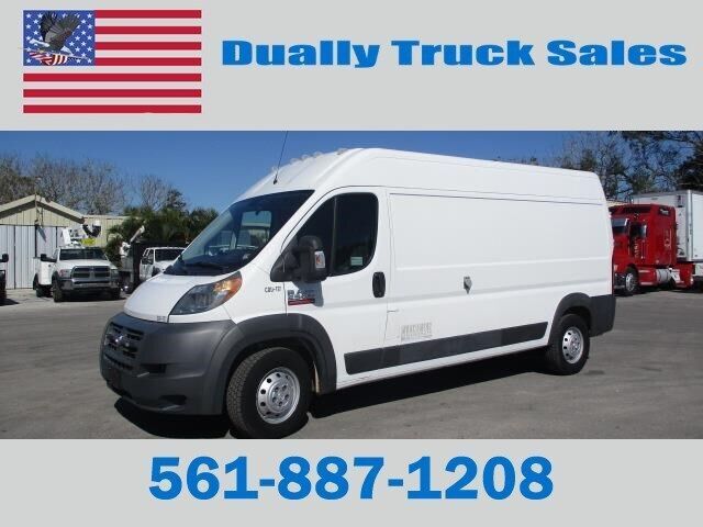 A white van is parked in front of a sign that says dually truck sales