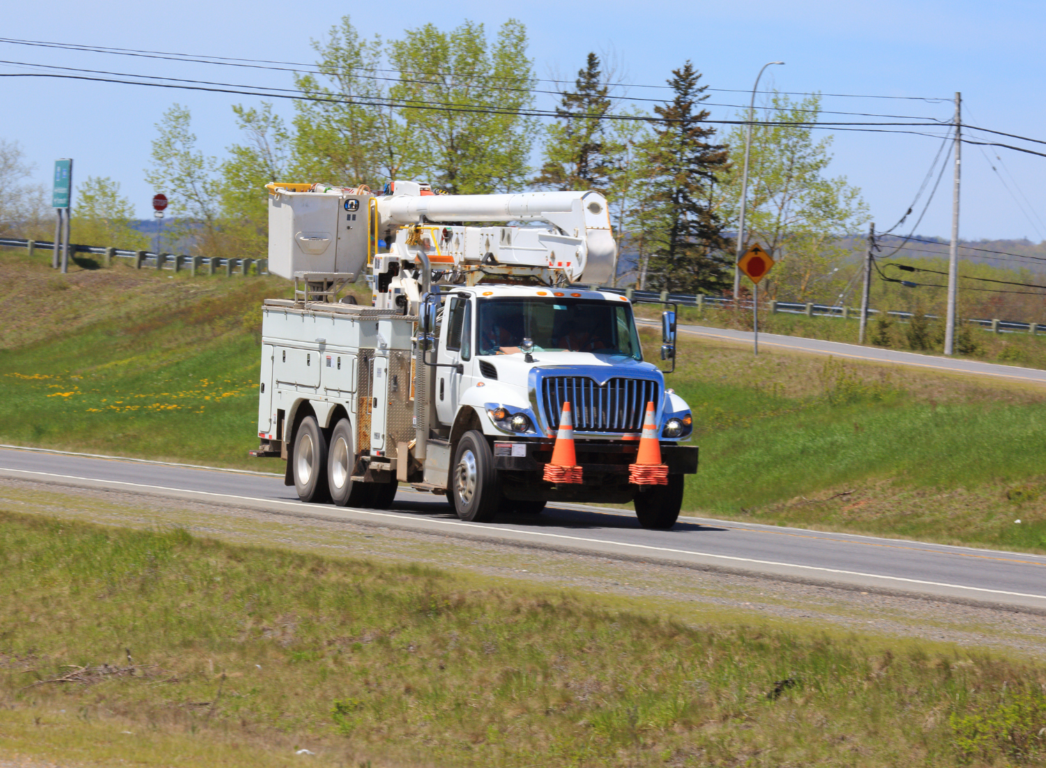 A white truck with orange cones on the front is driving down a road