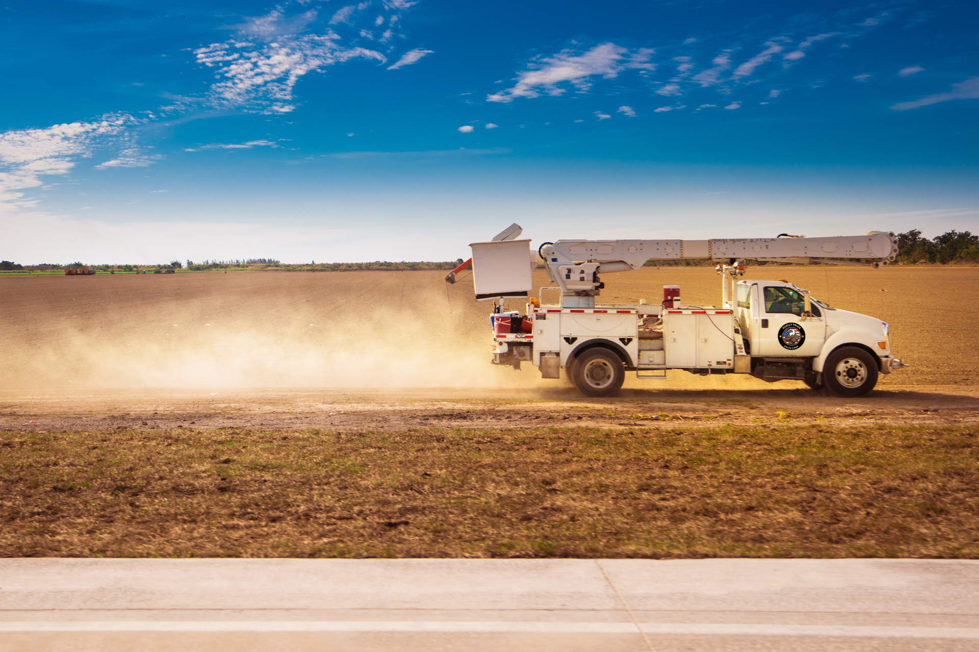 A white truck is driving down a dirt road next to a field.