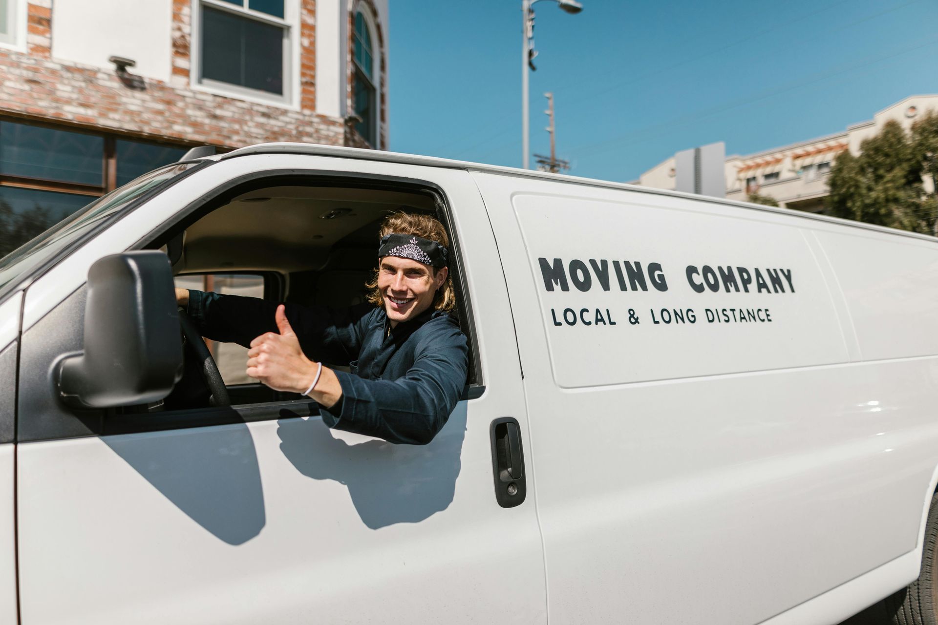 A man is driving a moving company van and giving a thumbs up.