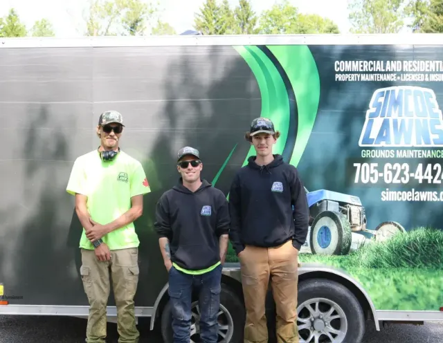 Three people stand in front of a trailer with